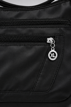 Zoom détaillé sur la poche zippée et le nylon satiné du sac, fond gris clair
