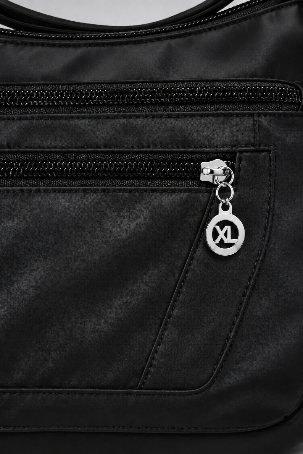 Zoom détaillé sur la poche zippée et le nylon satiné du sac, fond gris clair