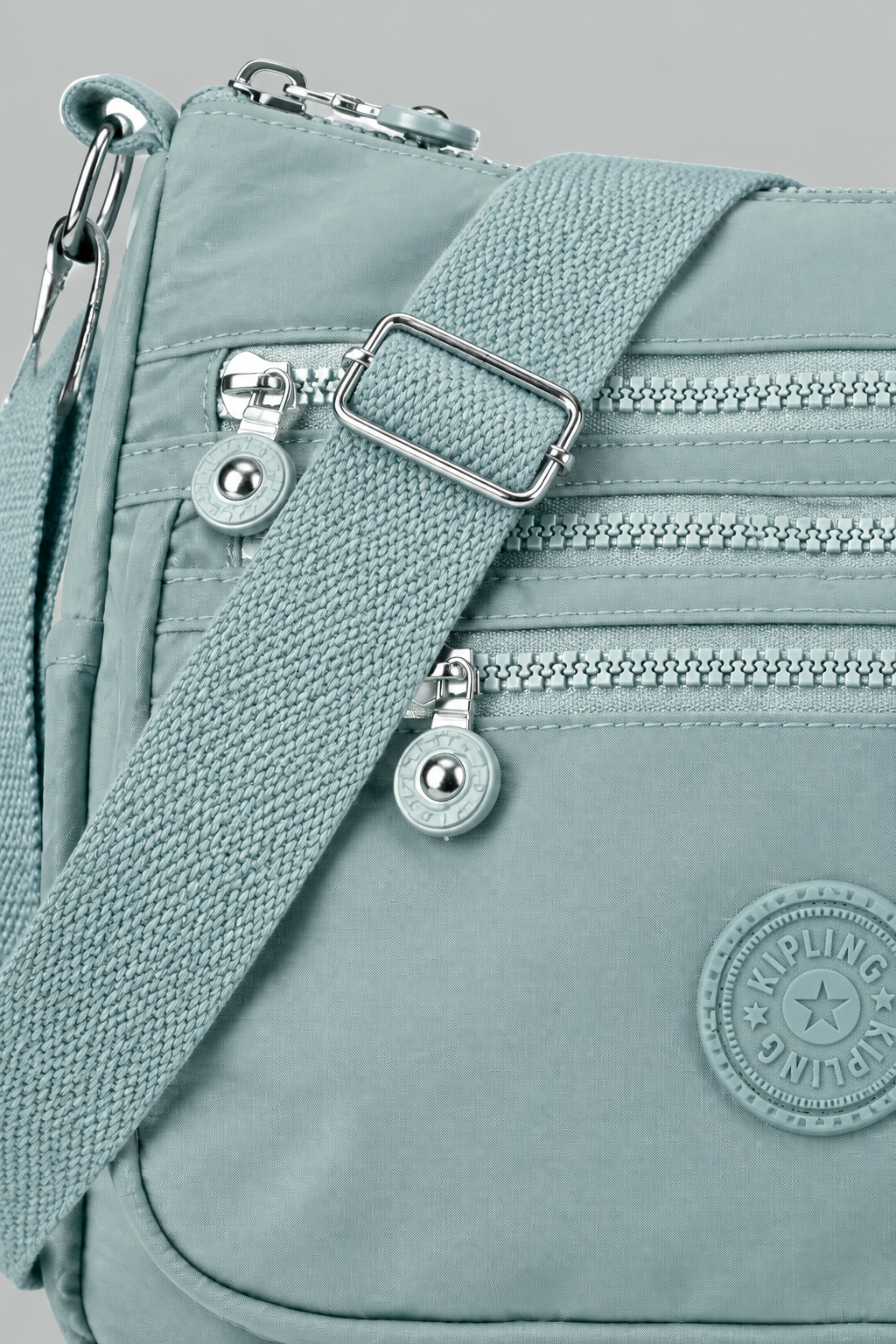 Zoom sur la matière nylon bleu du sac Lara, zips argentés et logo, fond gris